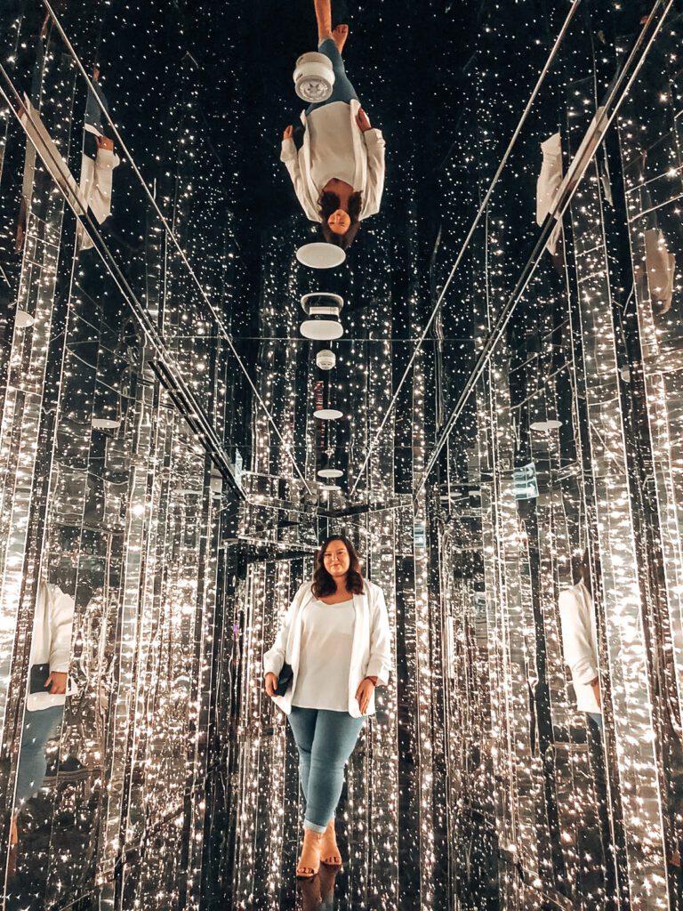hannah stood in a mirrored room wearing a white cami top and blue jeans