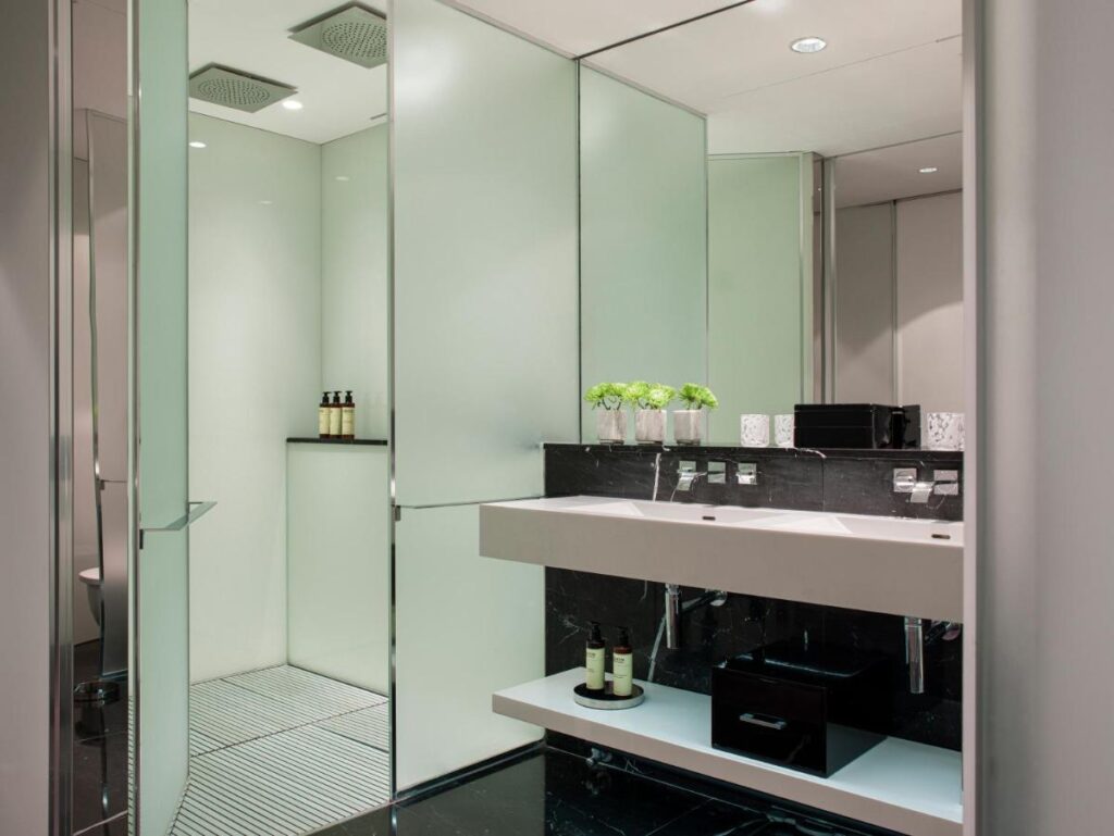this photo shows a photo of a double sink in a bathroom with a large mirror above both sinks. A black marble back splash with products lined up ontop