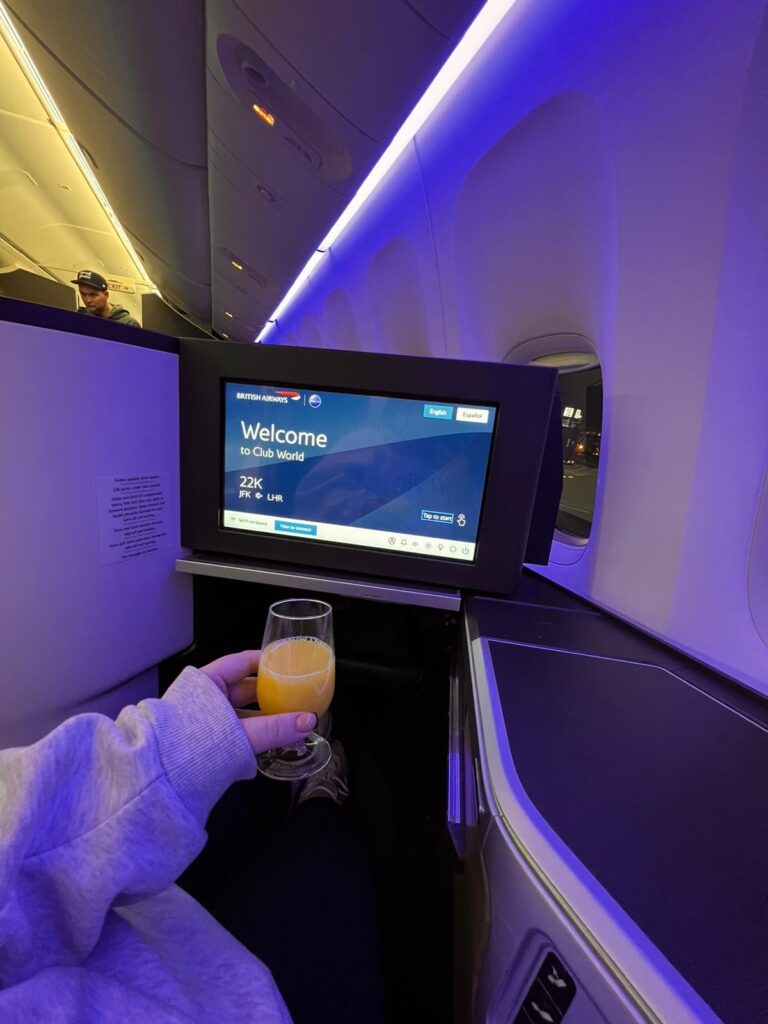 photo of the tv in the business class seat, with hannah holding a glass of orange juice up infront of the TV
