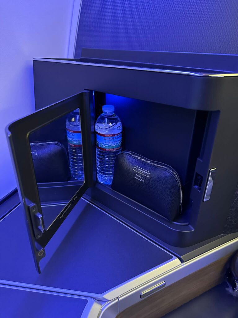 the business class storage space, holding a cosmetic bag and bottle of water